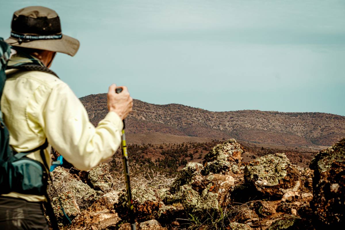 Hiker checking wristwatch altimeter while standing on mountain ridge during sunrise, demonstrating altimeter-based route planning in action